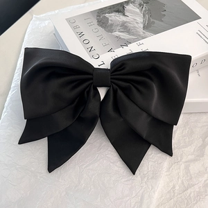 Detailed close-up of a large black satin double-layered bow hair clip on a white background