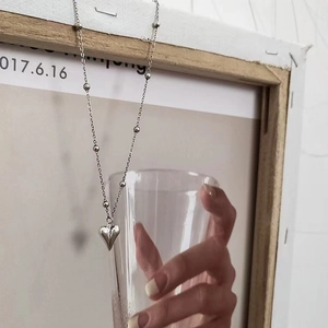 Detailed view of silver heart pendant on a beaded chain draped over a wooden frame