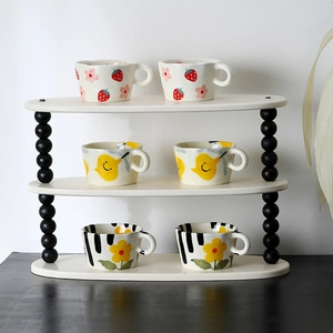 Three-tier oval shelf with black pillars holding cute strawberry and floral ceramic mugs