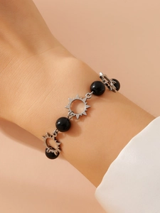 Detail of silver sun pendant and black beads on a minimalist bracelet worn by model