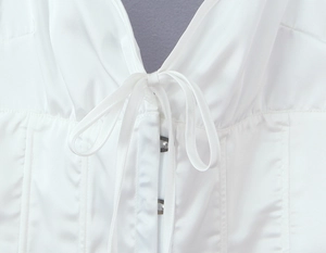 Detalle de top blanco efecto seda con elegante lazo al cuello y hebilla de metal