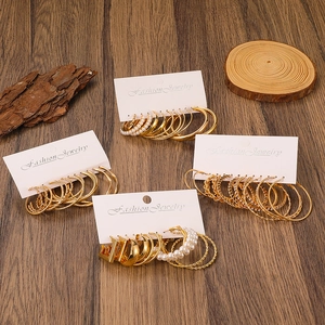 Detail of gold-tone earrings set with pearl accents and textured hoops on wood background