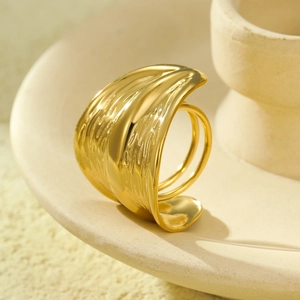 Golden wide stainless steel ring with irregular texture on a vintage ceramic plate