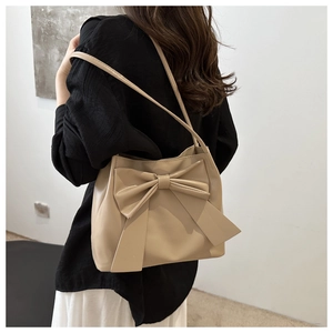Detail view of khaki tote bag with oversized bow decoration on leather surface