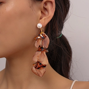 Close-up of brown acrylic petal tassel earrings with pearl studs worn by a model