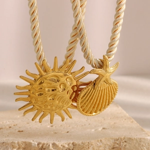 Detail of 18K gold-plated sun and seashell pendants on a braided rope necklace