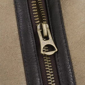 Detail of vintage bronze metal zipper with dark brown leather trim on suede jacket