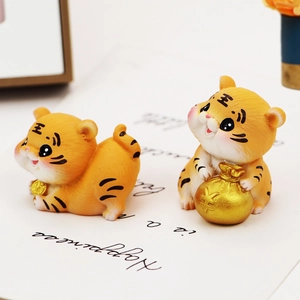 Macro view of two yellow resin tiger figurines with gold coin and money bag ornaments