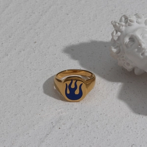 Artistic close-up of a 18K gold-plated ring with blue flame oil dripping on a white surface
