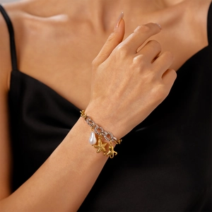 Detail of gold octopus and starfish charms on a pearl bracelet worn on a wrist