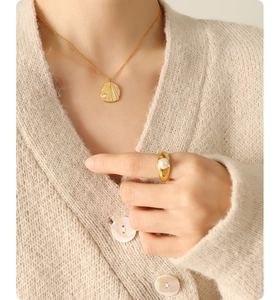 Detailed close-up of golden pearl necklace and wide ring on a model with beige knitwear