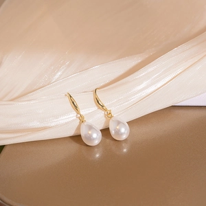 Elegant gold-plated teardrop pearl earrings displayed on textured light gold silk fabric