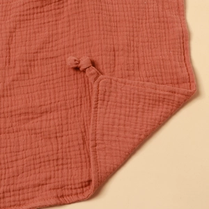 Macro detail of terracotta double-layer cotton gauze baby blanket with knotted corner