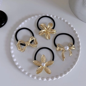 Close-up of four gold floral and bow hair ties with pearls in a white ceramic dish