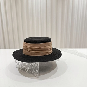 Close-up of black straw sun hat with elegant khaki pleated ribbon on rippled glass