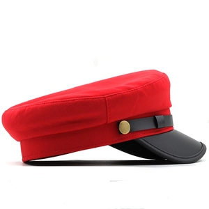 Detail view of red fabric military cap with black leather brim and gold buckle accents
