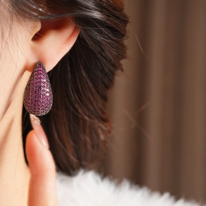 Detailed close-up of teardrop pavé earrings with rose red crystals and gunmetal finish