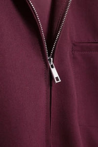 Detail of silver metal zipper and textured twill fabric on a burgundy lapel jacket