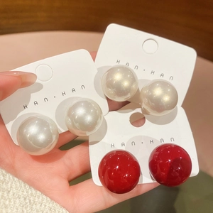 Macro detail of large round pearl stud earrings in white, cream, and glossy red colors