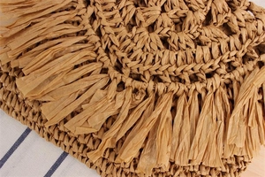 Detailed close-up of handmade straw weaving texture and bohemian tassels on a summer bag