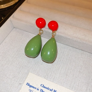 Macro shot of resin drop earrings with red studs and green pendants on velvet