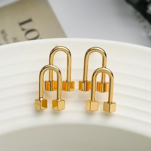 Minimalist gold plated geometric arch stud earrings with cube charm displayed on white ceramic
