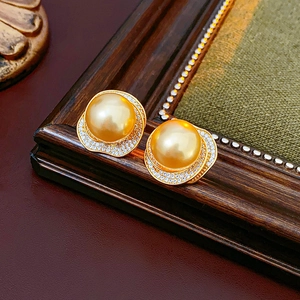 Detail of vintage gold pearl earrings with zircon inlay on dark wood and green fabric