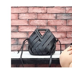 Macro shot of black woven leather handbag with triangular handle against a red brick wall