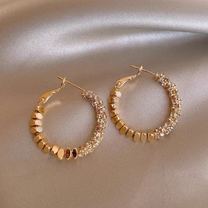 Macro detail of gold-plated hoop earrings with pavé crystals on champagne satin background