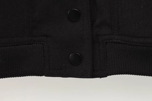 Detail einer schwarzen Twill-Jacke mit Druckknöpfen und geripptem elastischem Saum
