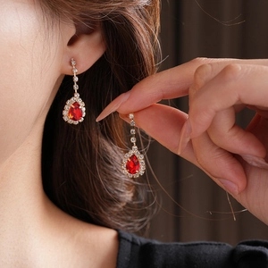 Macro shot of gold water-drop earrings with red gemstones and crystals on model