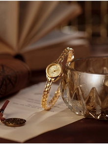 Detailed macro view of a vintage mini round gold watch leaning against textured glass