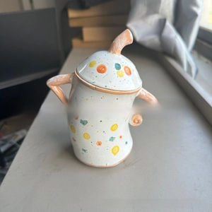 Detail of hand-painted colorful polka dots and arm-shaped handles on a white ceramic jar
