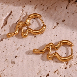Macro view of gold plated wavy liquid metal earrings on a beige stone texture
