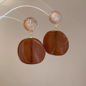 Close-up of brown and champagne resin earrings with golden metal rings on gray background