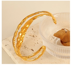 Artistic close-up of gold plated layered lava texture cuff bracelet on stone and glass