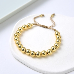 Close-up of golden beaded bracelet with adjustable woven cord on marble base