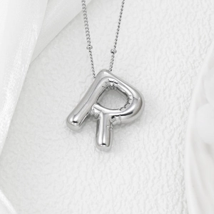 Macro detail of puffy silver balloon letter R pendant with textured fold effects