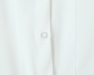 Close-up of white lace dress featuring a translucent button and precise stitching detail