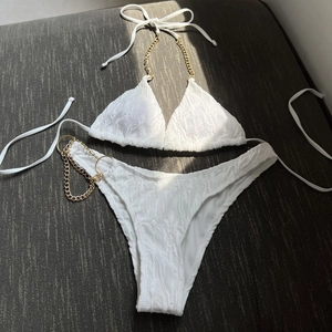 White textured bikini set with golden chain straps and side ring details on a grey surface