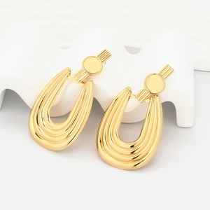 Detailed view of gold geometric earrings with ribbed U-shaped pendants on white podiums