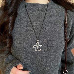 Detail of silver flower heart pendant necklace worn on a grey knit sweater background