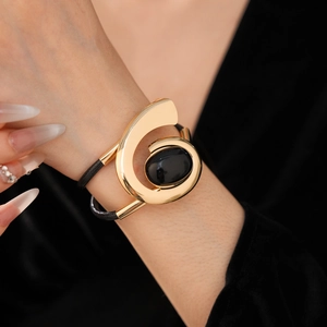 Detail of a large gold G-shaped cuff bracelet with black oval gem on a leather strap