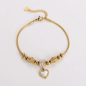 Detail of gold snake chain bracelet with heart pendant and sparkling spacers on white background