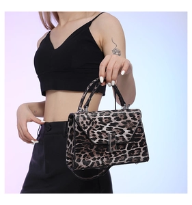 Detail of trendy leopard print handbag with metal lock and black top handle worn by model