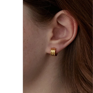 Close-up of triple-layered golden metal hoop earrings worn on a model's ear