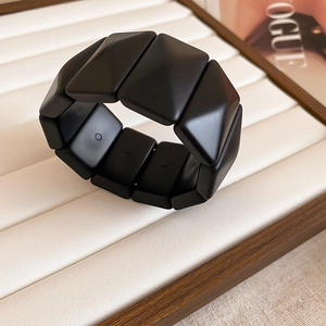 Detail of a matte black geometric pyramid bracelet on a white textured display stand