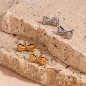Detailed view of bow-shaped stud earrings in polished gold and silver on stone