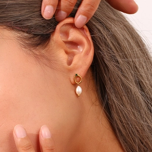 Close-up of gold hoop earring featuring a green gemstone and natural freshwater pearl