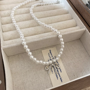 Gros plan d'un collier de perles avec pendentif noeud argenté sur un écrin vintage